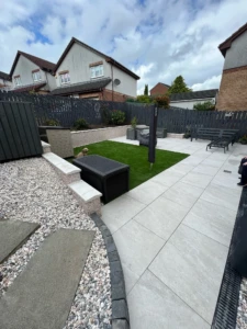 "Transform your outdoor space with a stunning porcelain patio, complete with a stylish retaining wall and luscious artificial grass. Create a perfect retreat in Denny for relaxation and enjoyment." A beautifully installed porcelain patio in Denny, featuring a retaining wall that seamlessly merges two levels into one. The patio is complemented by the addition of artificial grass, creating a low-maintenance and visually appealing outdoor space."