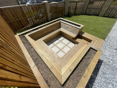 "Creating an Oasis in Dunfermline: Our sunken seating area installation features a rustic sleeper frame, cozy timber deck board seating, and elegant cream porcelain tiles at the center. The perfect spot to relax and enjoy the outdoors. #OutdoorLiving #Dunfermline" "Inviting sunken seating area in Dunfermline featuring sleeper frame, timber deck board seating, and cream porcelain tiles in the center. Completed with topsoil and turf for a lush and comfortable outdoor space."